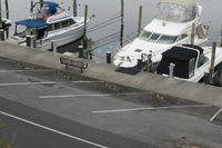 a motor boat docked in an empty marina with two boats parked by the dock and a parking lot on the side of the road