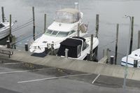 a motor boat docked in an empty marina with two boats parked by the dock and a parking lot on the side of the road