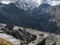 a person riding a motorbike on a rocky mountain road with snow capped mountains in the background