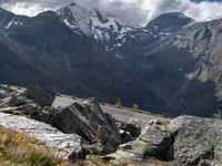 a person riding a motorbike on a rocky mountain road with snow capped mountains in the background