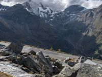 a person riding a motorbike on a rocky mountain road with snow capped mountains in the background