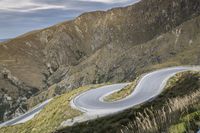 a person on a mountain top rides a motorcycle down a winding road in front of a mountain range