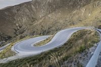 a person on a mountain top rides a motorcycle down a winding road in front of a mountain range