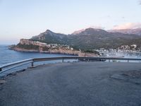 the back end of a motorcycle resting on a bike path near an ocean shore and mountains