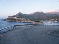 the back end of a motorcycle resting on a bike path near an ocean shore and mountains