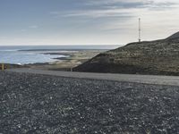 a motorcycle that is sitting on a gravel road by the ocean with mountains in the background