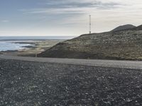 a motorcycle that is sitting on a gravel road by the ocean with mountains in the background