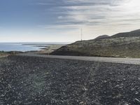 a motorcycle that is sitting on a gravel road by the ocean with mountains in the background