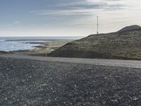 a motorcycle that is sitting on a gravel road by the ocean with mountains in the background