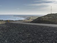 a motorcycle that is sitting on a gravel road by the ocean with mountains in the background