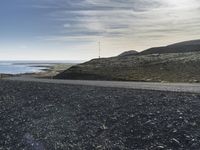 a motorcycle that is sitting on a gravel road by the ocean with mountains in the background