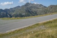 a motorcycle on a country road in front of mountains near grass and bushes, in front of a large mountain