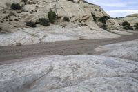 a motorcycle is driving down the desert by some boulders and boulders of various sizes, patterns and textures