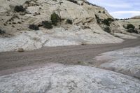 a motorcycle is driving down the desert by some boulders and boulders of various sizes, patterns and textures