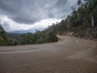 a motorcycle driving on a dirt road surrounded by trees and mountains in the rain clouds