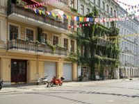 a motorcycle is driving along a city street near large buildings and gardens and greenery