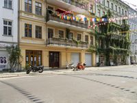 a motorcycle is driving along a city street near large buildings and gardens and greenery