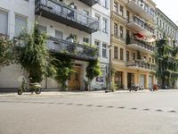 a motorcycle is driving along a city street near large buildings and gardens and greenery