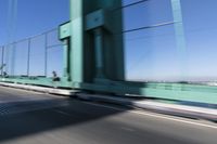 a person driving a motorcycle on a bridge on a blue day, the blurry bridge is in the background