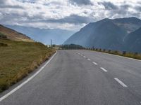 a motorcycle driving along a curvy country side road in front of a mountain range