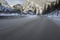 a motorcycle driving down the road in the mountains near snow on the ground with a small village on either side
