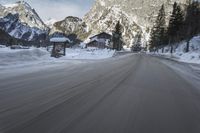 a motorcycle driving down the road in the mountains near snow on the ground with a small village on either side