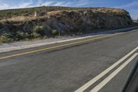 a motorcycle driving down the road in front of a rocky mountain side with clouds and sky