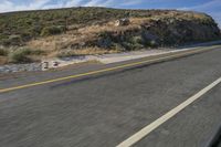 a motorcycle driving down the road in front of a rocky mountain side with clouds and sky