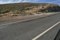 a motorcycle driving down the road in front of a rocky mountain side with clouds and sky