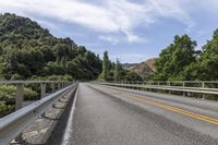 a motorcycle is driving through a rural roadway near some trees and mountains above a mountain