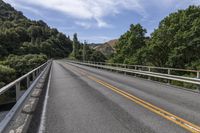 a motorcycle is driving through a rural roadway near some trees and mountains above a mountain