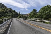 a motorcycle is driving through a rural roadway near some trees and mountains above a mountain