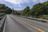 a motorcycle is driving through a rural roadway near some trees and mountains above a mountain