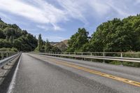 a motorcycle is driving through a rural roadway near some trees and mountains above a mountain