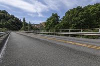 a motorcycle is driving through a rural roadway near some trees and mountains above a mountain