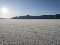 a lone motorcycle is driving along a salt plain at sunset near mountains in the distance