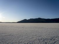 a lone motorcycle is driving along a salt plain at sunset near mountains in the distance