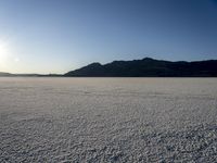 a lone motorcycle is driving along a salt plain at sunset near mountains in the distance