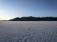 a lone motorcycle is driving along a salt plain at sunset near mountains in the distance