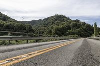 a motorcycle drives along a highway with green trees in the background and mountains on one side