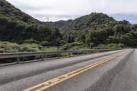 a motorcycle drives along a highway with green trees in the background and mountains on one side