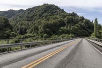 a motorcycle drives along a highway with green trees in the background and mountains on one side