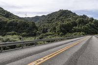 a motorcycle drives along a highway with green trees in the background and mountains on one side