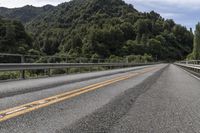 a motorcycle drives along a highway with green trees in the background and mountains on one side