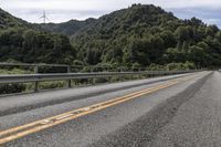 a motorcycle drives along a highway with green trees in the background and mountains on one side