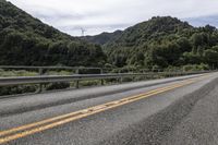 a motorcycle drives along a highway with green trees in the background and mountains on one side