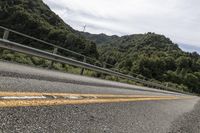 a motorcycle drives along a highway with green trees in the background and mountains on one side