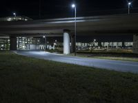 a motorcycle parked under a bridge at night time, near a grassy field below which is a highway