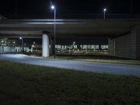 a motorcycle parked under a bridge at night time, near a grassy field below which is a highway