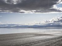 a lone motor cycle is parked on a beach at low tide waterside with mountains in the background